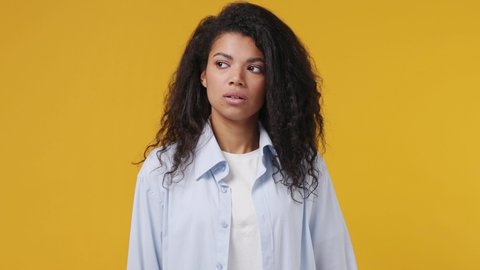 Confused worried sad upset shocked young african woman curly hair 20s years old wears blue white t shirt looking around suspects think misdoubt isolated on yellow color wall background studio portrait