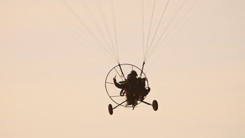 Close-up of paramotor trike under parachute flying towards camera, against sunset sky view. Tandem motor powered paragliding at twilight. 