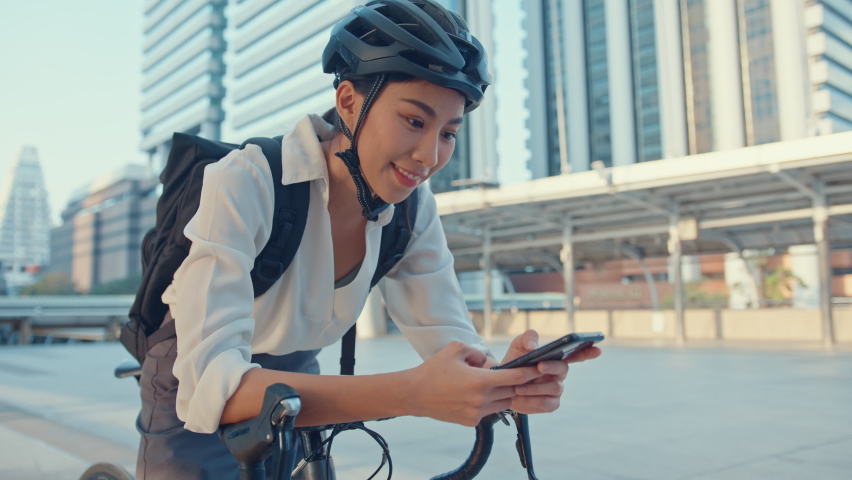 Smile asian businesswoman with backpack use smart phone look camera in city stand at street with bike go to work at office. Sport girl use phone for work. Commute to work, Business commuter in city. Royalty-Free Stock Footage #1071274372
