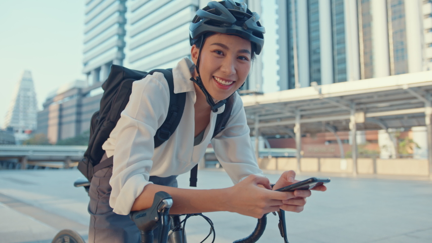 Smile asian businesswoman with backpack use smart phone look camera in city stand at street with bike go to work at office. Sport girl use phone for work. Commute to work, Business commuter in city. | Shutterstock HD Video #1071274372
