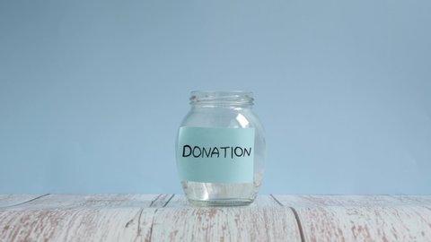 Hand throwing coins in transparent jar with inscription donation. Coins are falling down inside glass jar. Saving money for donation