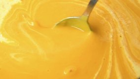 Cream of roasted pumpkin soup recipe. Step 23. Close-up view of person mixing liquid cream and almost ready pumpkin cream soup using spoon. Side view. Slow motion video. Home cooking theme.