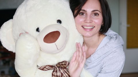 Active cheerful woman hugging with big teddy bear at home. Portrait of happy mother with short hair holding big teddy toy and saying hello for childen.