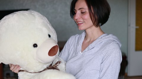 Active cheerful woman dancing with big teddy bear at home. Portrait of happy mother with short hair holding big teddy toy.