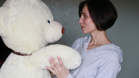 Active cheerful woman dancing with big teddy bear at home. Portrait of happy mother with short hair holding big teddy toy.