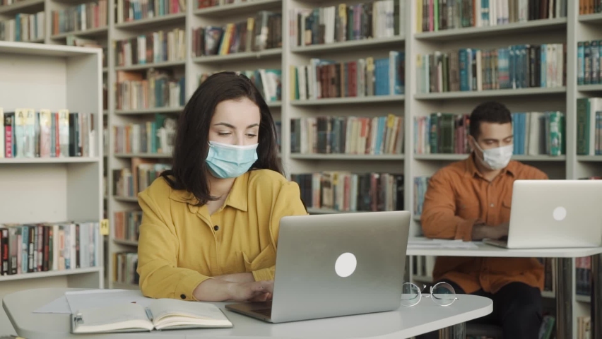 university students wearing face mask and sitting with books and laptop in library, social distance in University.