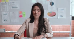 POV of A young, confident, beautiful Asian professional businesswoman sitting in the conference room, making conference video calls and explain the data in the papers. Business Meeting concept.