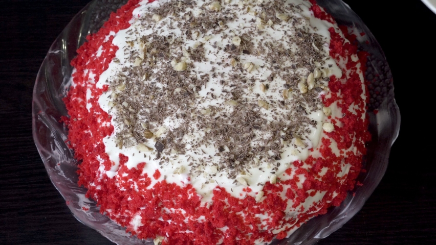 The pastry chef prepares a beautiful cake and sprinkles it with grated nuts and chocolate. Red cake on a black table. Concept. Small business during quarantine. Close-up. Top view. Faceless. 4K.
