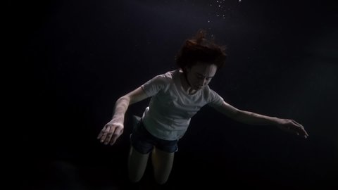 adult woman is sinking in depth of sea or river, closed eyes, breathless body, subaquatic shot