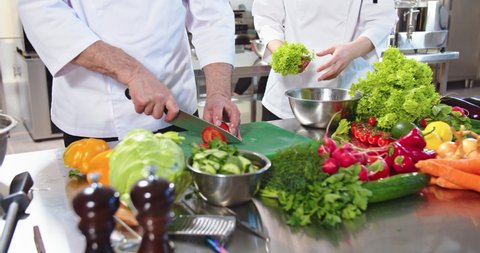 Close up of male hands cutting tomato working in restaurant. Chef working in restaurant kitchen, slicing vegetables, preparing salad. Workflow, employees at cafeteria. Cookery, cook profession concept