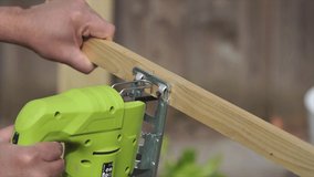 Person Cutting a Small Piece of Wood With a Drawn Line in Half With a Green Jigsaw