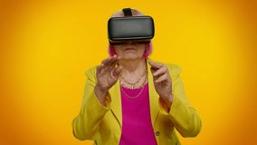 Senior granny gray-haired woman using virtual reality futuristic technology VR app headset helmet to play simulation 3D 360 video game, drawing. Orange studio background. Elderly grandmother pensioner