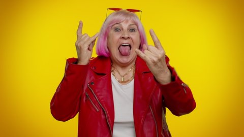 Overjoyed stylish elderly granny woman showing rock n roll gesture by hands, cool sign, shouting yeah with crazy expression, dancing, emotionally rejoicing in success. Senior mature old grandmother