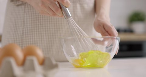 Young woman stirring eggs with hand mixer, close-up. Cooking at home kitchen. Slow motion