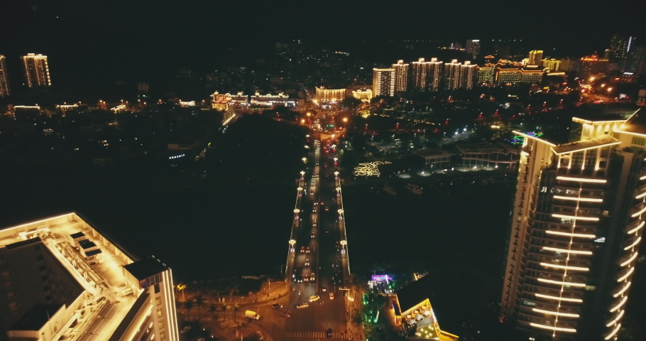 Illuminated bridge road at night cityscape slow motion aerial. Cars drive on traffic highway. Business centre. Buildings neon light. Urban lifestyle at twilight. Sanya town, Hainan Island, China, Asia