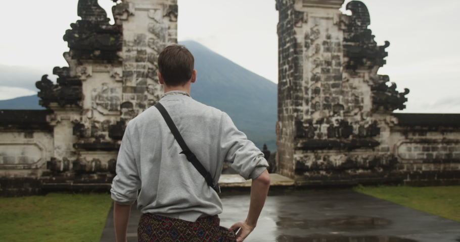 Close up dolly medium view of a white male tourist walking towards the Gates of Heaven tourist attraction in Pura Penataran Agung Lempuyang temple and Mount Agung volcano in Bali