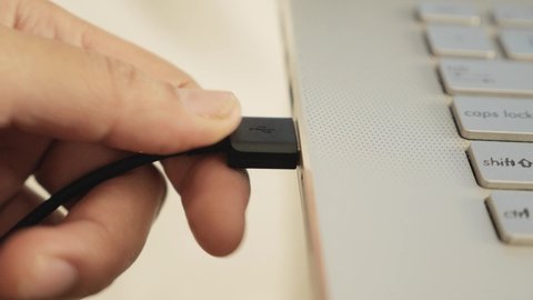 Close up of hand inserting plugging data cable into usb port in laptop; data transfer concept