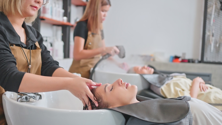 Caucasian young woman lying down and close eye on salon washing bed getting hair washed by professional stylist. Beautiful customer feeling relax while hairdresser massaging head at beauty barber shop | Shutterstock HD Video #1071325945