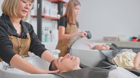 Caucasian young woman lying down and close eye on salon washing bed getting hair washed by professional stylist. Beautiful customer feeling relax while hairdresser massaging head at beauty barber shop