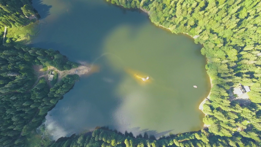 Top down aerial view of big lake with clear blue water between high mountain hills covered with dense evergreen forest.