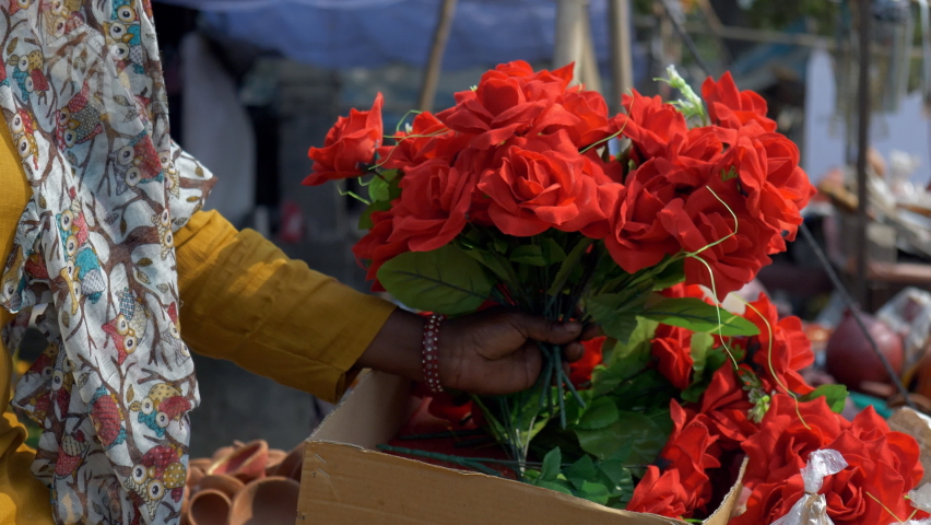 A lot of beautiful flowers and other home decors in the market on Indian festivals. Indian lady holding a bunch of artificial red roses in her hands for sale at a roadside stall in Delhi NCR, India