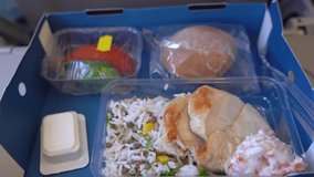 Closeup view 4k stock video footage of woman eating food on board of flying plane. Paper box full of plastic trays with different food: rice, chicken, salad, cucumbers, tomatos, bun and butter packed