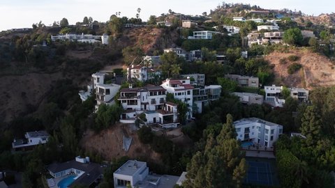 Panning and rising aerial shot of Beverly Hills mansions dotting the hillside. 4K