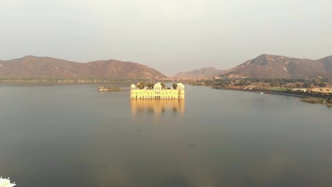 Jal Mahal unique beauty amidst the vast Sagar Lake, reflected on the water surface in Jaipur, Rajasthan, India - Aerial push in fly-over shot