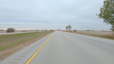 POV driving on a interstate highway past flat, harvested fields on a cloudy winter day in rural western Illinois