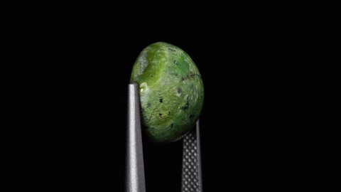 natural green opal gemstone in the tweezer on the background