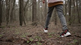 The girl walks in the park in the spring. A tree without leaves has no grass and a child walks in the woods. Slow motion 4K video of a teenager in nature dressed in jeans and a jacket.