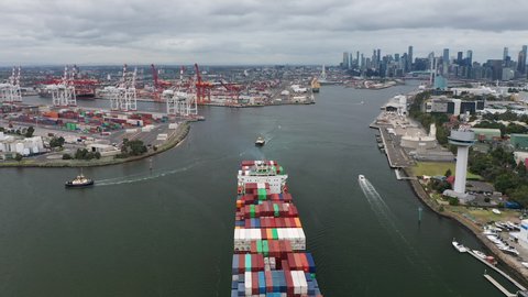 Melbourne, Australia - Apr 16, 2021: Aerial revealing shot of cargo ship leaving port in Melbourne with view of CBD