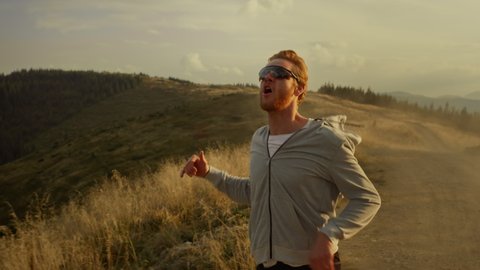 Tired jogger running in mountain landscape. Smiling guy raising hands outdoor. Happy man jumping high in air. Excited male athlete enjoying success outdoor.