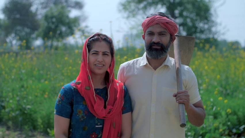 Indian married woman with Duppata on head smiling and standing with husband - Farmer couple. Rural couple in traditional wear cheerfully posing for the camera standing in their green farm outdoors Royalty-Free Stock Footage #1071343294
