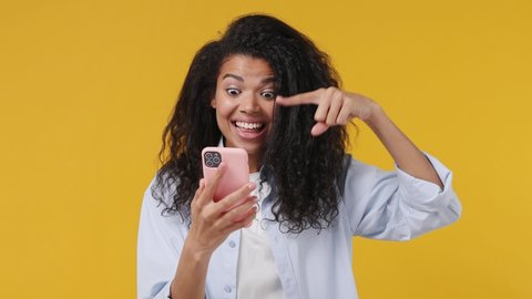 Happy young african woman wears blue white t shirt hold use mobile cell phone typing say wow yes just found out great big win news doing winner gesture isolated on yellow color wall background studio