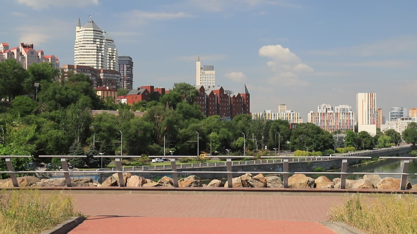Cars go along the street against the background of buildings, towers, skyscrapers, park in the city  Dnepropetrovsk, Dnipro, Ukraine. Beautiful view from Monastyrsky Island in spring and summer Royalty-Free Stock Footage #1071344320