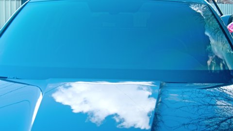 The reflection of clear sky on black car hood, bonnet after car wash, ceramic coat. Car detail and paint protection concept. Shiny car background. Top view.