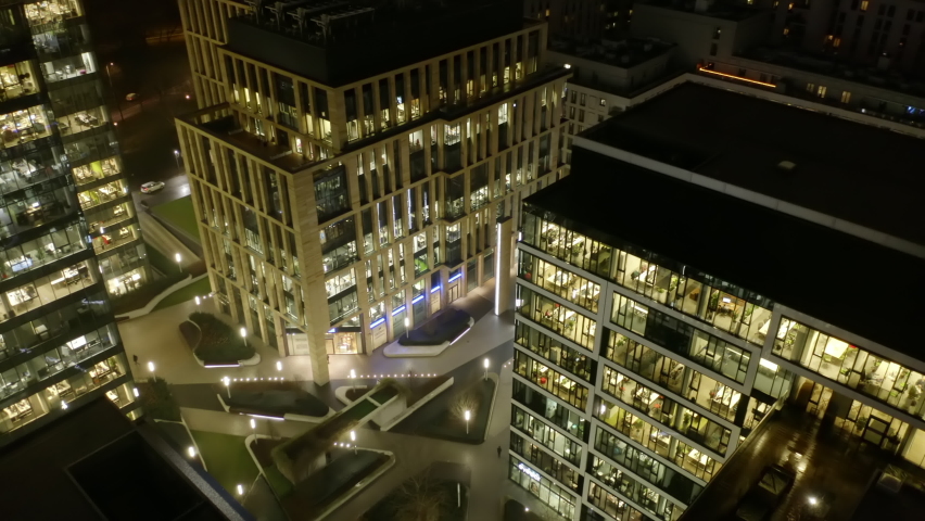 A cinematic view from a drone of the night skyscrapers with office windows in the evening in winter. Warsaw, Poland. The drone flies past the windows of offices at night, people in the windows