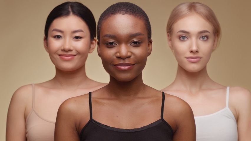 Diverse beauty. Happy african american lady with dental braces smiling widely to camera, posing with asian and caucasian female friends over beige background Royalty-Free Stock Footage #1071348904