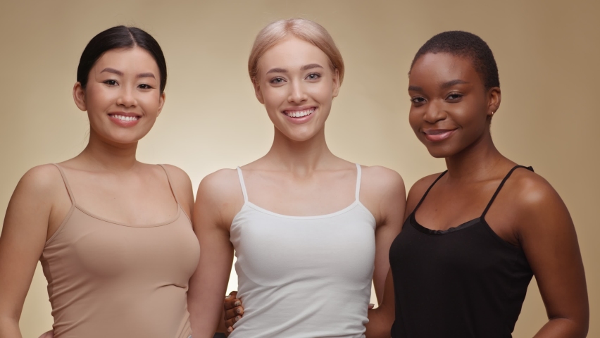 Different female beauty. Three happy diverse young women embracing together and laughing to camera, beige studio background, slow motion Royalty-Free Stock Footage #1071348907