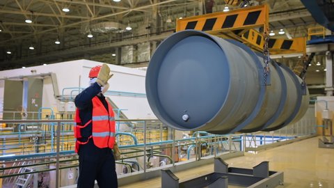 Chemical Production Facility. A Male Worker wearing Protective gloves and Supervising the Process of Placing the Big Chemical Barrel While the Crane is Moving the Barrel Sideways. Industrial Plant