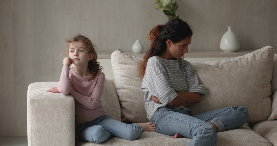 Gloomy mom and daughter sit on sofa turned away from each other. Sulky little girl feels offended not talk and looks at mom while sit together on couch. Upbringing problems, quarrels in family concept Royalty-Free Stock Footage #1071353806