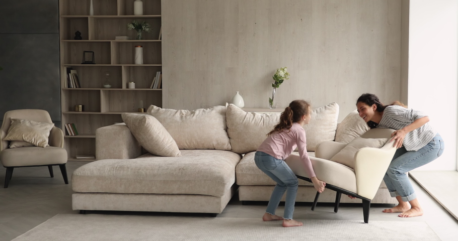 Woman and daughter rearranging furniture in spacious living room. Mom and kid move cozy armchair together, give high five enjoy weekend at new modern house. Happy homeowners family relocation concept Royalty-Free Stock Footage #1071353809