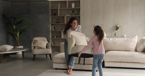 Woman and daughter rearranging furniture in spacious living room. Mom and kid move cozy armchair together, give high five enjoy weekend at new modern house. Happy homeowners family relocation concept