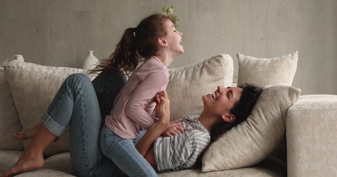 Latina mother caucasian daughter diverse family play funny active game on sofa in living room, loving parent tickling adopted kid girl express caress, bonding and love. Fun and leisure at home concept