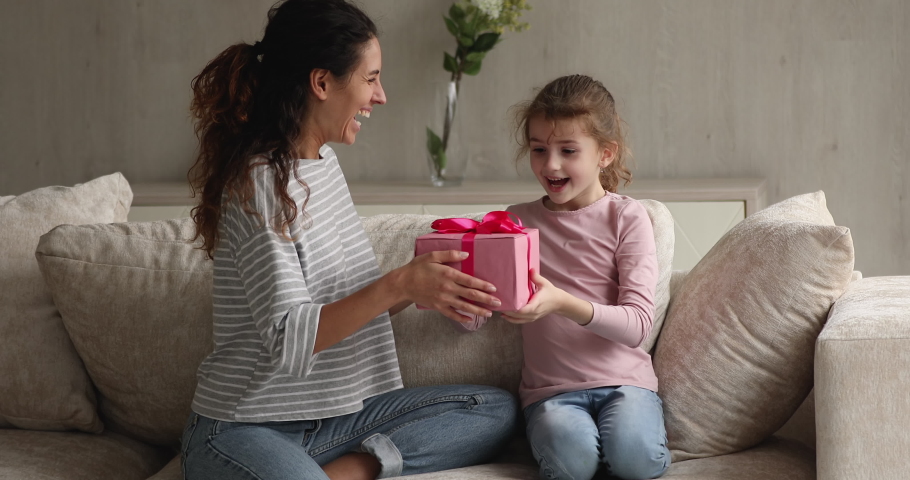 Mom makes gift for little daughter gives box congratulates birthday. Preschool girl cover eyes with hands anticipate mommy surprise, receiving pink package feel happy. Life events celebration concept Royalty-Free Stock Footage #1071353905