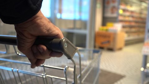 senior hands pushing trolley in supermarket, department store or shopping mall. lifestyle concept. outside the home. blur background with copy space. blurred video. film grain.