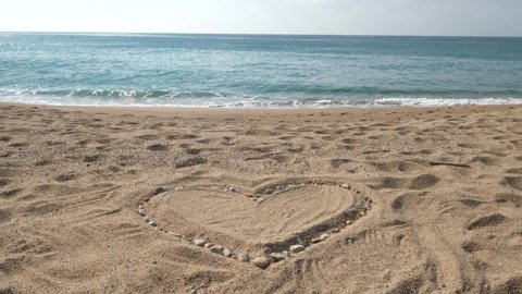 Heart on the beach in the sand with small rocks and shells. Empty sunny beach with heart in the sand. Perfect for love stories. 
