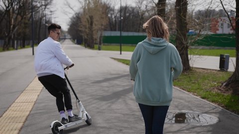 A beautiful couple of young people ride in the park on electric scooters