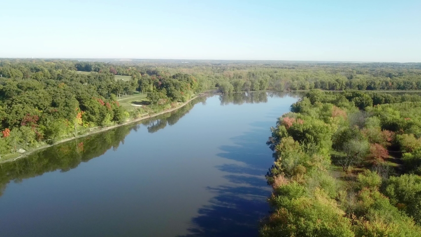 Low angle, slow drone view following the Iowa River water trail on a sunny late summer day near Iowa City Iowa; bike trail and golf course are visible